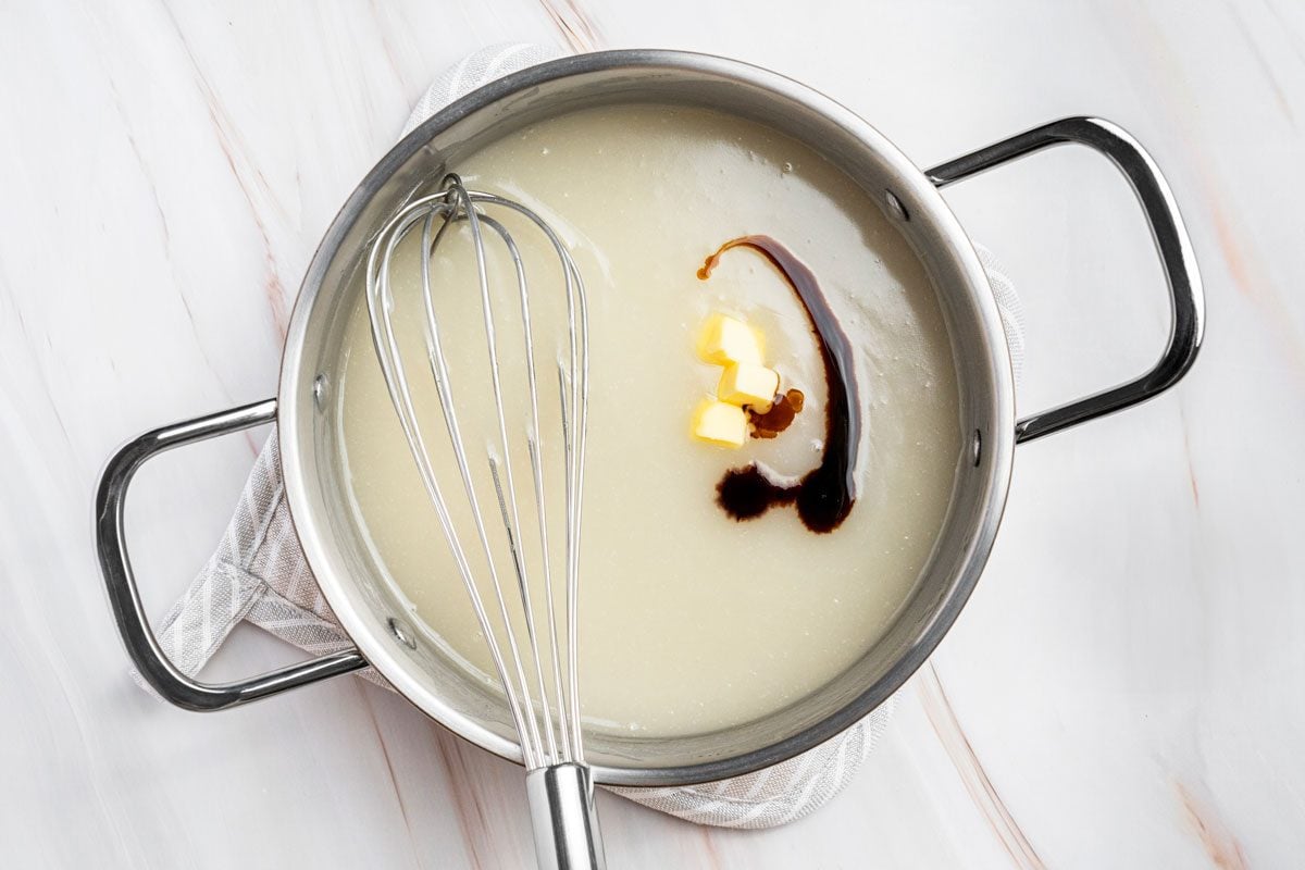 Overhead shot of stir in butter and vanilla; whisk tool; Cool to room temperature; all set on a marble surface;