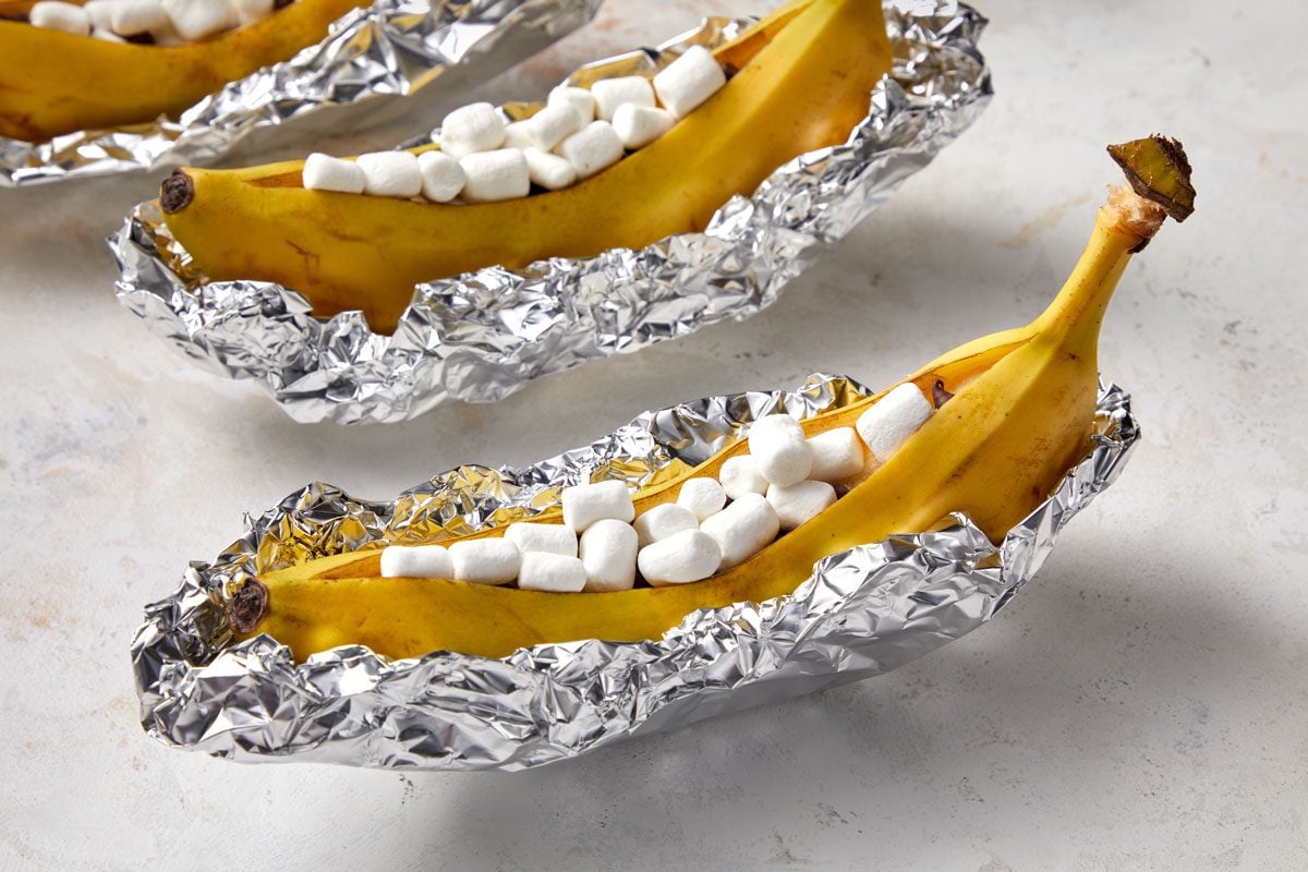 Close shot of Crimp and shape four pieces of heavy-duty foil around bananas; forming boats; Grill, covered, over medium heat until marshmallows melt and are golden brown 5-10 minutes; all set on a marble surface;
