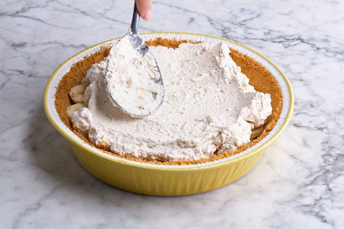 3/4 angle view shot of spoon whipped cream over the bananas; Refrigerate at least three hours or overnight; all set on a marble textured surface