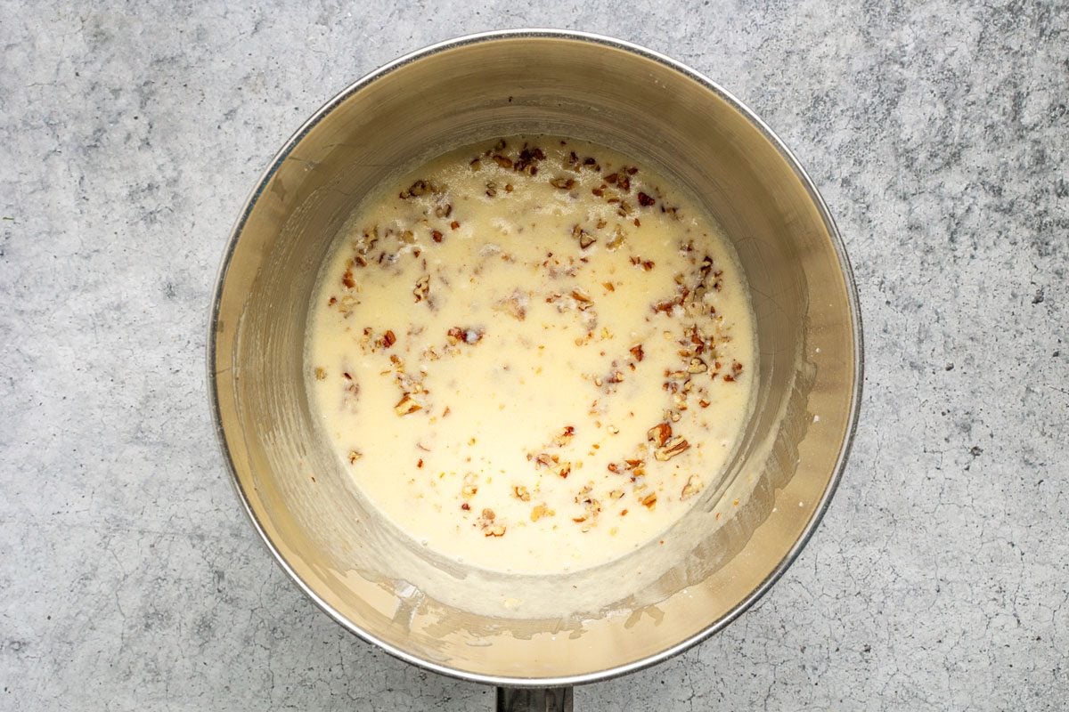 A metal saucepan containing a creamy sauce with visible specks of cooked bacon, sitting on a light gray textured surface.