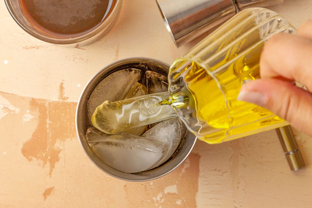 Overhead shot of a cocktail shaker filled with ice; add espresso and Licor 43; shake until well-chilled and frothy; fill a rocks glass with ice; strain cocktail into the glass; garnish with an orange peel; serve immediately; all set on a painted surface;