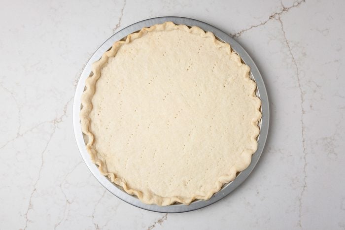 Overhead shot of roll out into a 14 inch circle; Place on an ungreased 12 inch pizza pan; Flute edges to form a rim; prick bottom of crust; Bake at 350 degree for 15 minutes; all set on a white texture marble surface