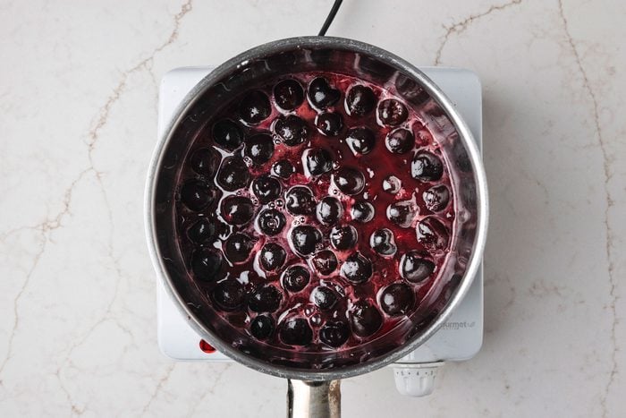 Overhead shot of a large saucepan combine sugar and cornstarch; stir in reserved juice until smooth; add cherries; Cook and stir over medium heat until mixture comes to a boil; Cook and stir 2 minutes longer; Remove from the heat; stir in butter; extract and food coloring; Cool to room temperature; all set on a white texture marble surface