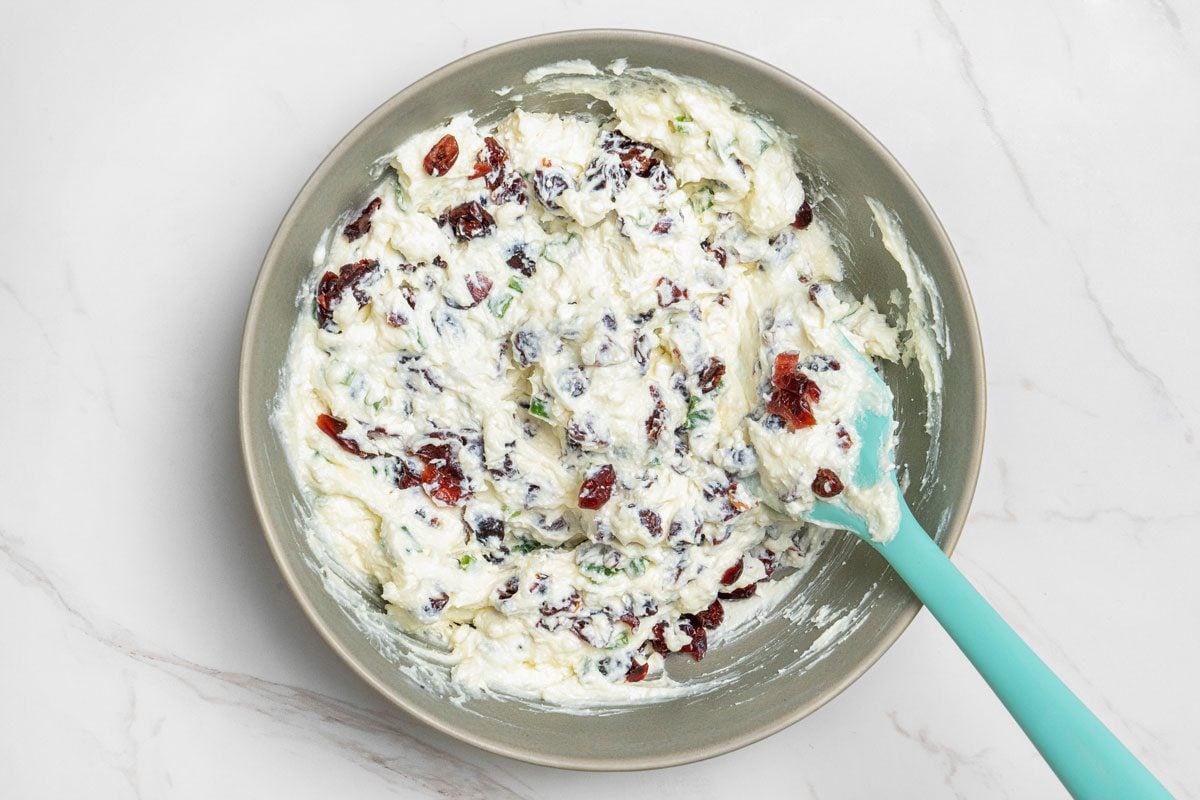 Overhead shot of stir in cranberries; spatula; all set on white marble surface;