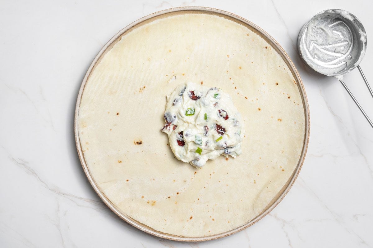 Overhead shot of spread about 1/2 cup mixture over each tortilla all set on a white marble surface;