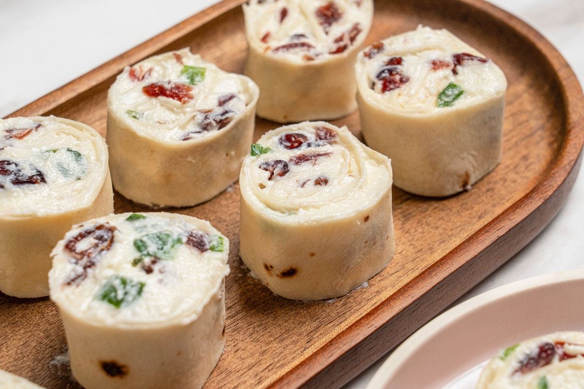 Closeup shot of Cranberry Feta Pinwheels placed on brown wooden platter; served on a small plate; all set on a white marble surface;