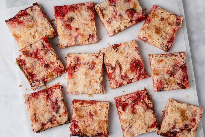 overhead shot of Twelve square pieces of Gluten Free Rhubarb Bars, are arranged on a white surface, showing a mix of red fruit and golden brown streusel topping