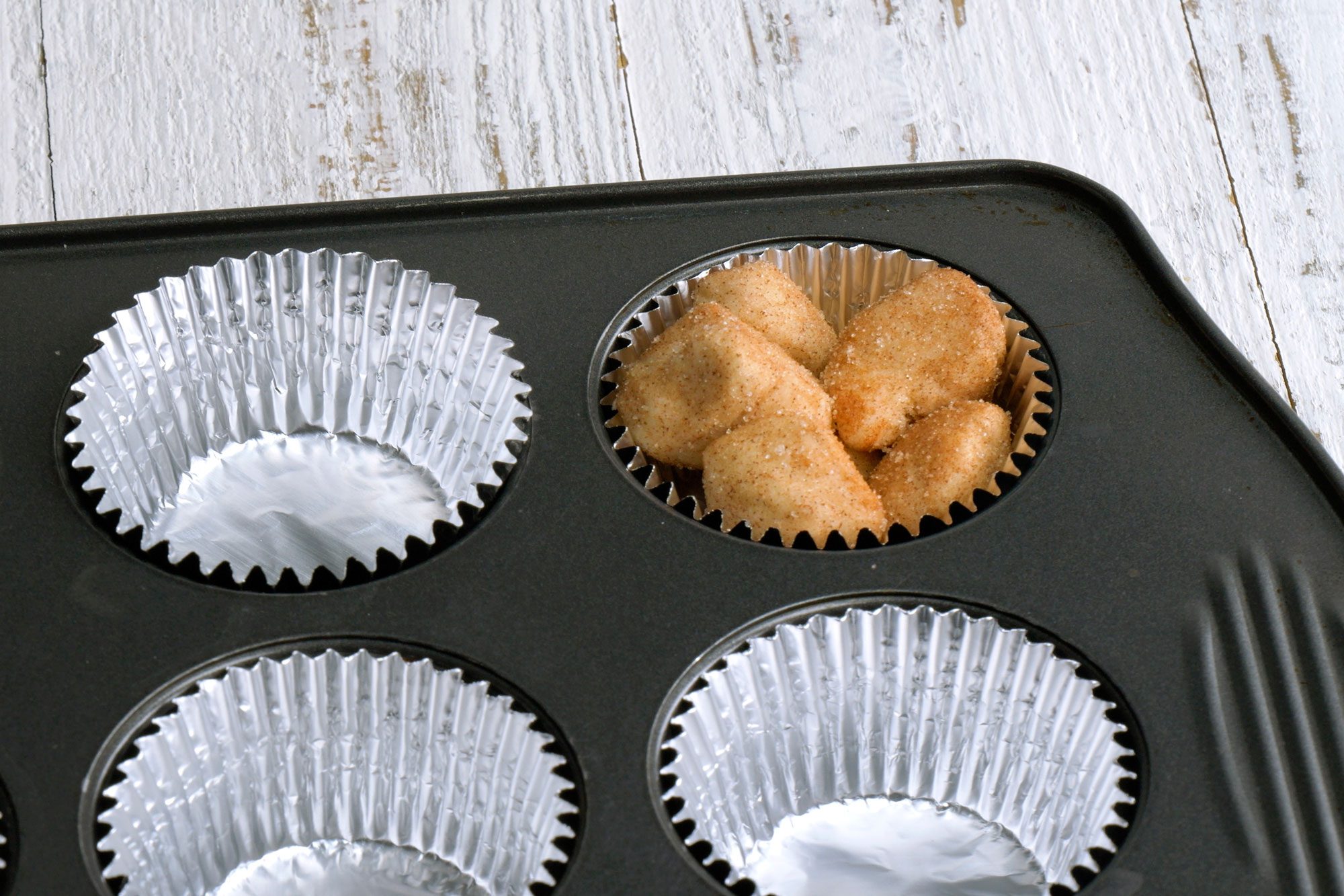 Toss biscuit pieces in cinnamon sugar; Divide pieces into prepared muffin tins