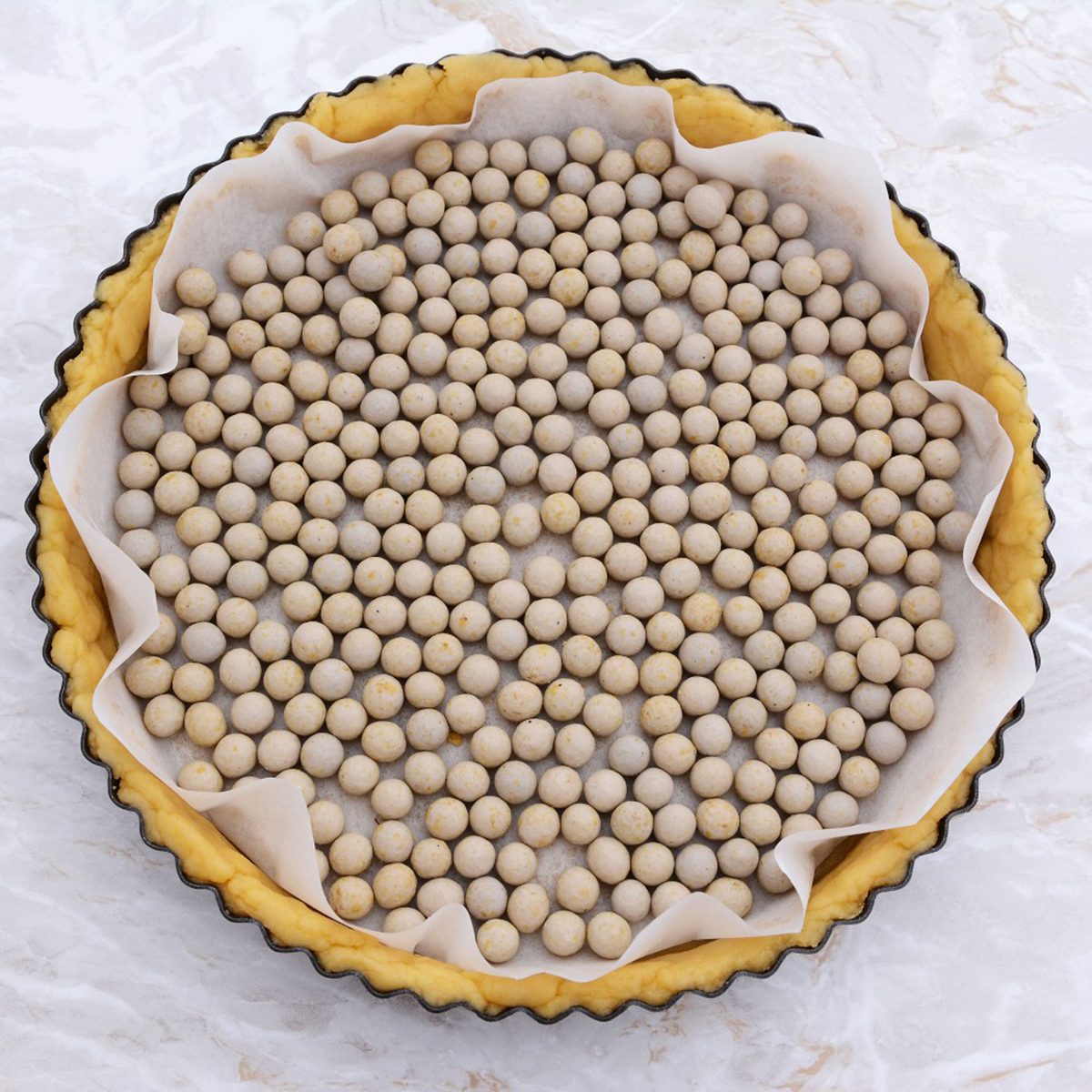 A pie crust lined with parchment paper is filled with ceramic baking beans, ready for blind baking in a tart pan.