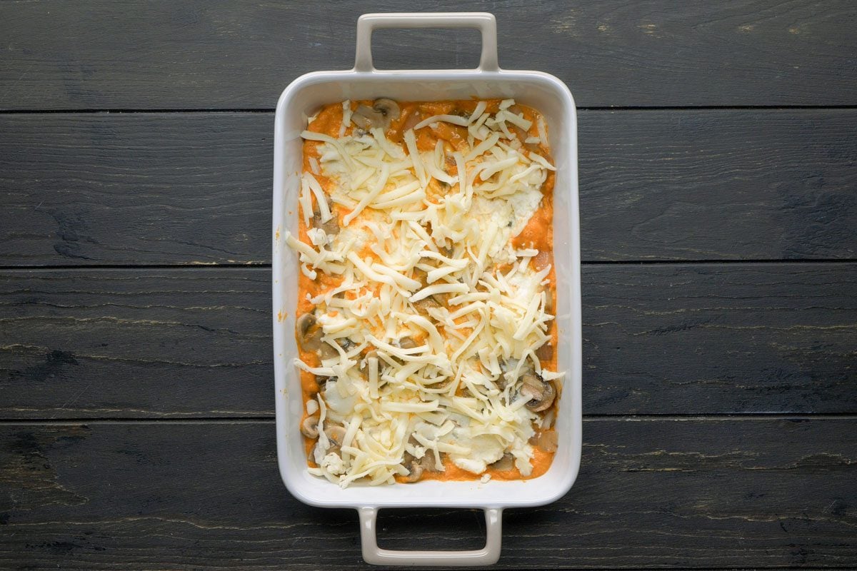 Top Shot of A rectangular white baking dish holds a cheesy casserole with sliced mushrooms on top; the dish sits on a dark wooden surface