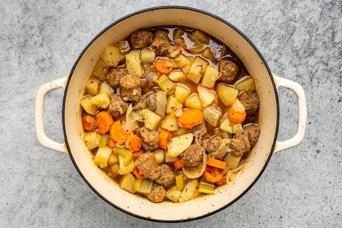 Overhead shot of a Dutch oven over medium heat; brown sausage; drain; Add the water; potatoes; carrots; celery; onions; Worcestershire sauce and seasonings; Bring to a boil; Reduce heat; cover and cook over low heat for 1 hour or until sausage is no longer pink and vegetables are tender; on a grey marble surface;