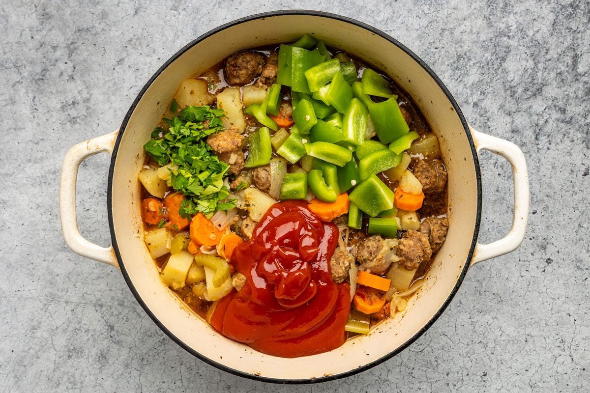 Overhead shot of the same dutch oven; Add the ketchup; green pepper and parsley; cook 12-15 minutes longer or until pepper is tender; Discard bay leaf; on a grey marble surface;