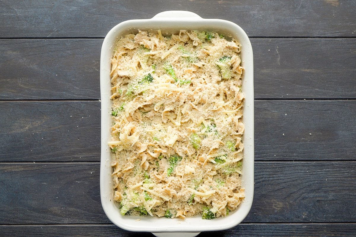 Top Shot of a white rectangular baking dish holds creamy pasta; broccoli; and shredded cheese, resting on a dark wooden surface; creating a delicious and inviting meal scene