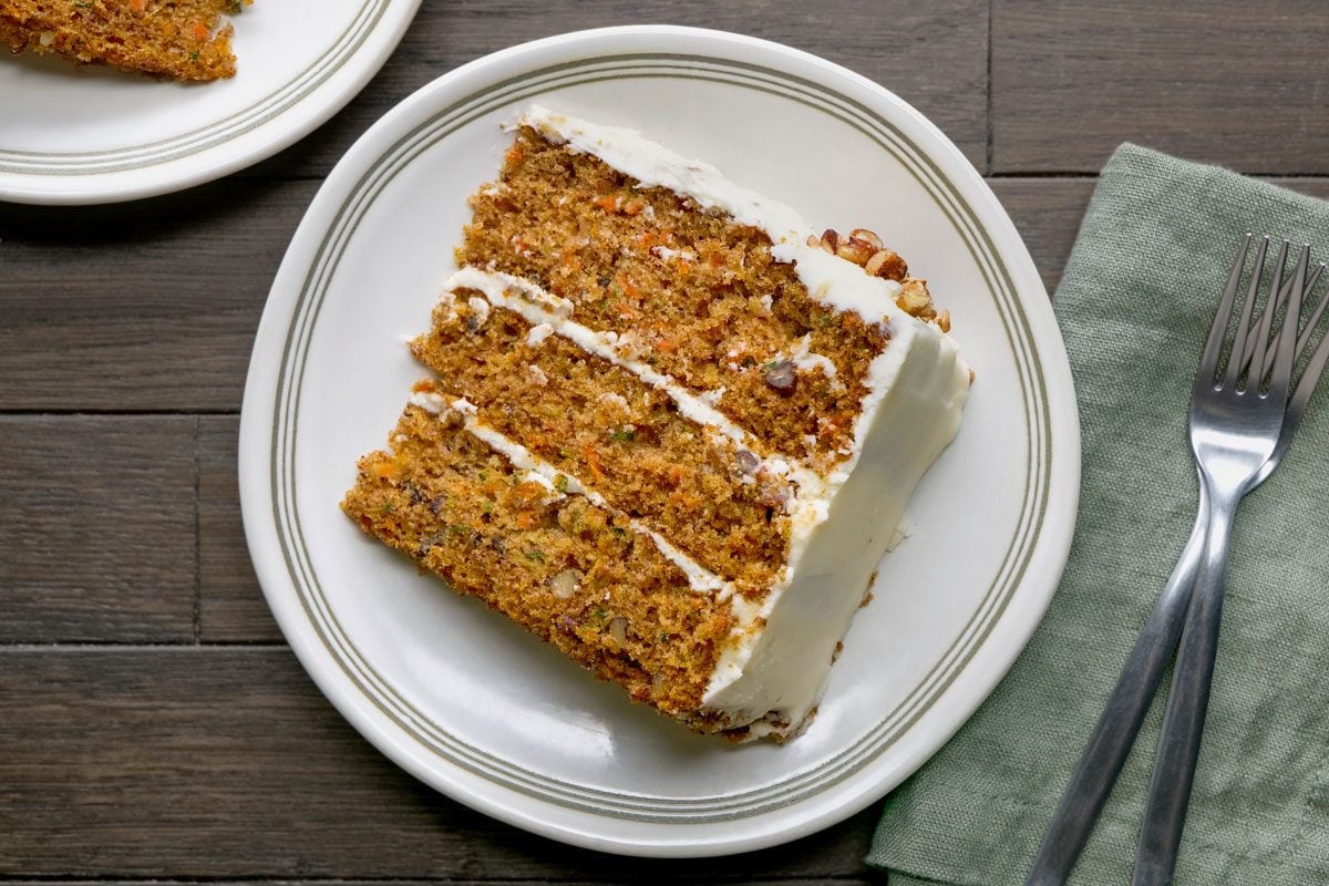 Top view of Zucchini Carrot Cake cut into slices and served on two plates; accompanied by two forks placed on a napkin; all arranged on a dark brown wooden surface;