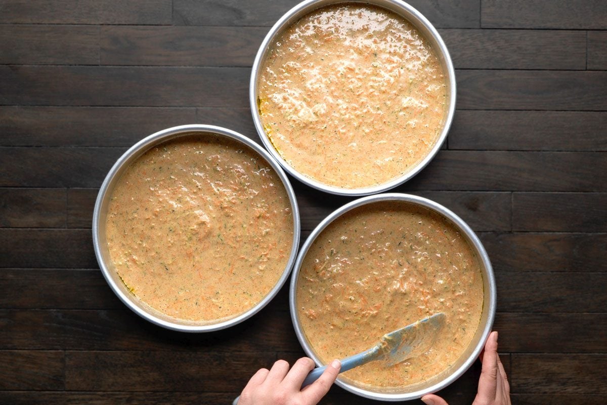 Overhead shot of Pour into three greased round baking pans; Bake at 350 degree for about 35 minutes or until top springs back when lightly touched; Cool 5 minutes before removing from pans; Cool thoroughly on a wire rack; all set on a dark brown wooden surface;