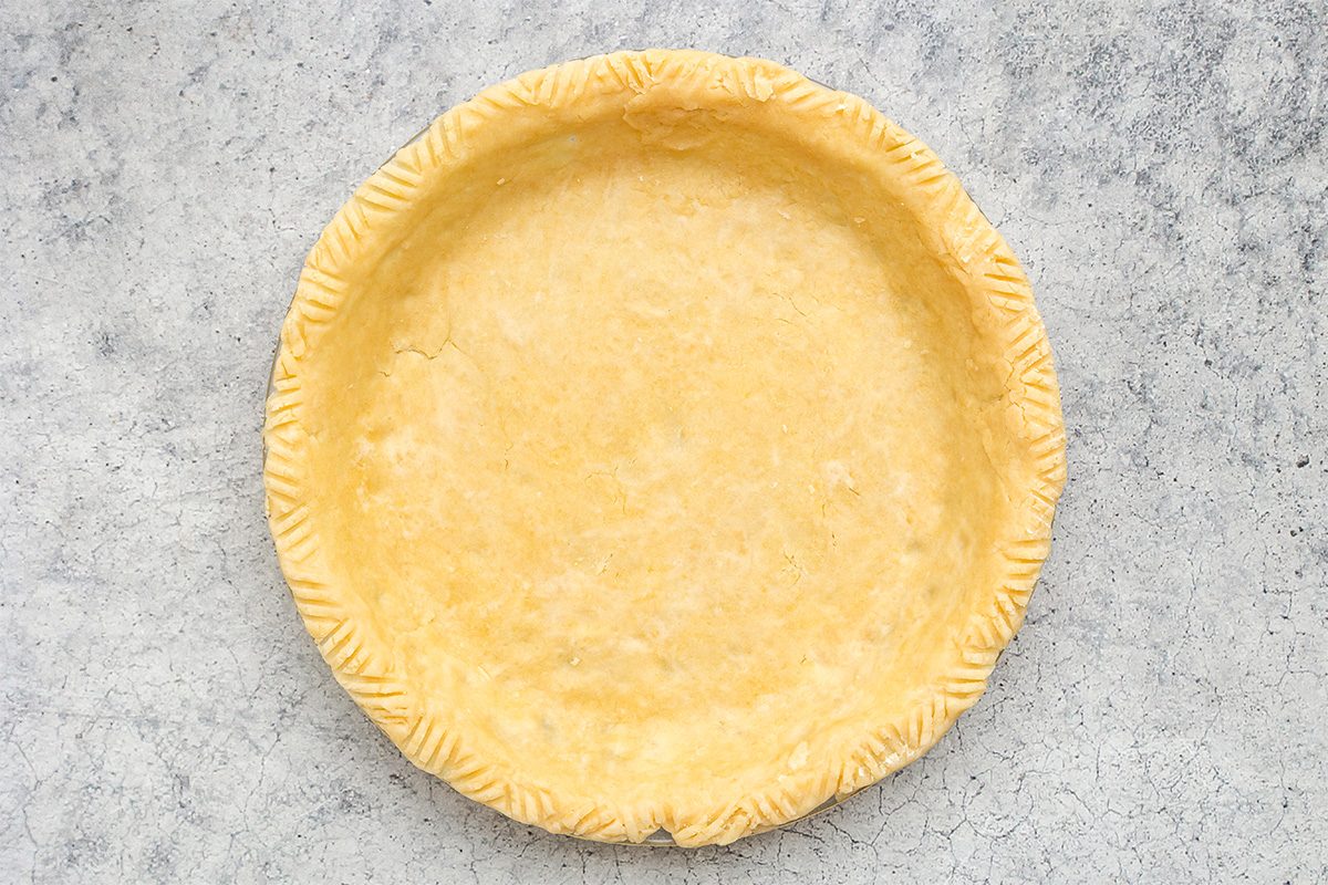A round, unbaked pie crust with crimped edges on a light gray, textured surface.