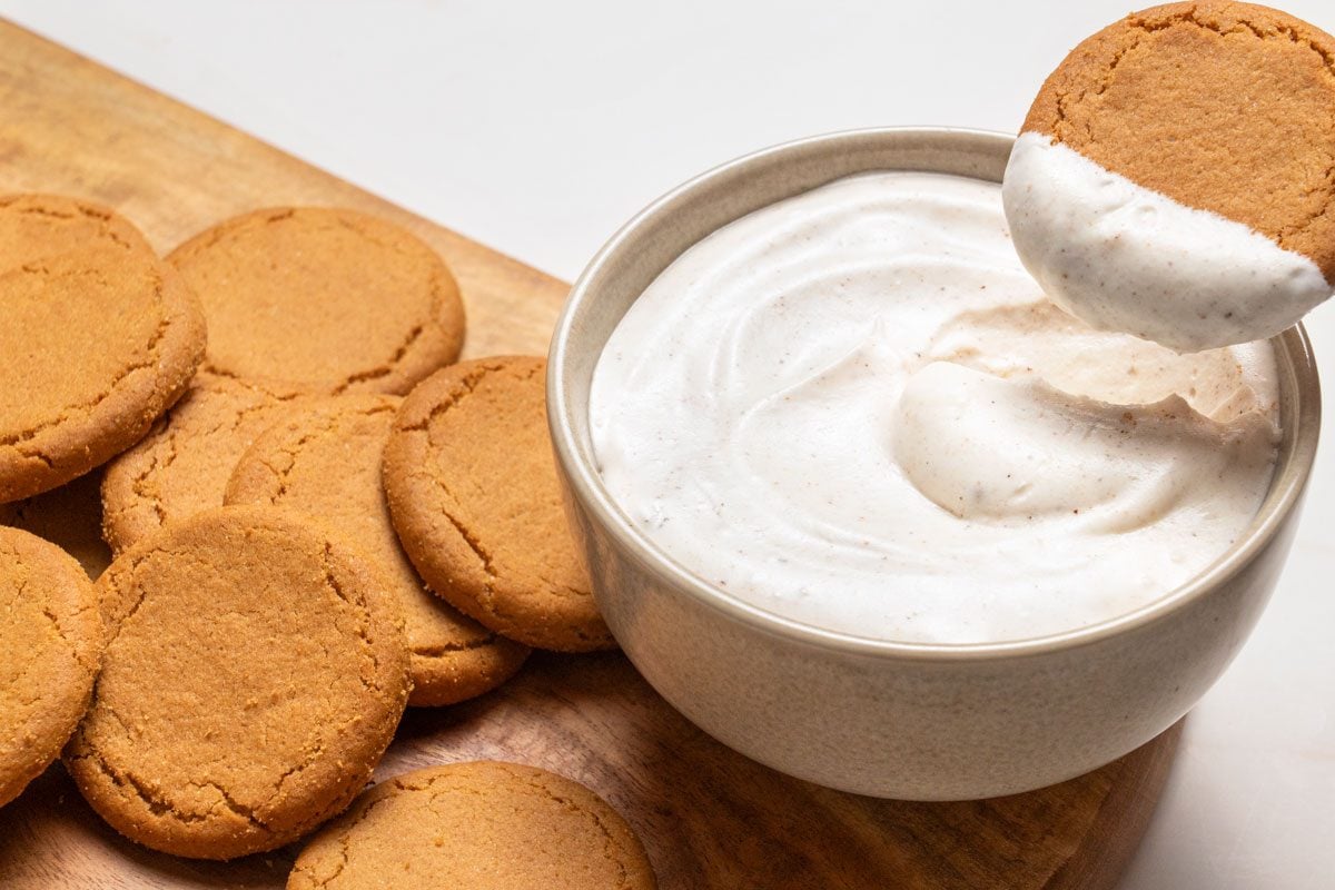 3/4 view angle shot of Gingersnap Dip served in a bowl with gingersnaps cookies; placed on a wooden platter or tray; all set on a white marble surface;