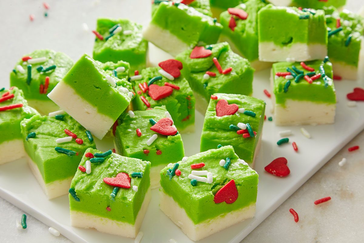 Closeup shot of Squares of white and green layered fudge are topped with red; green and white sprinkles and heart shaped decorations arranged on a white surface