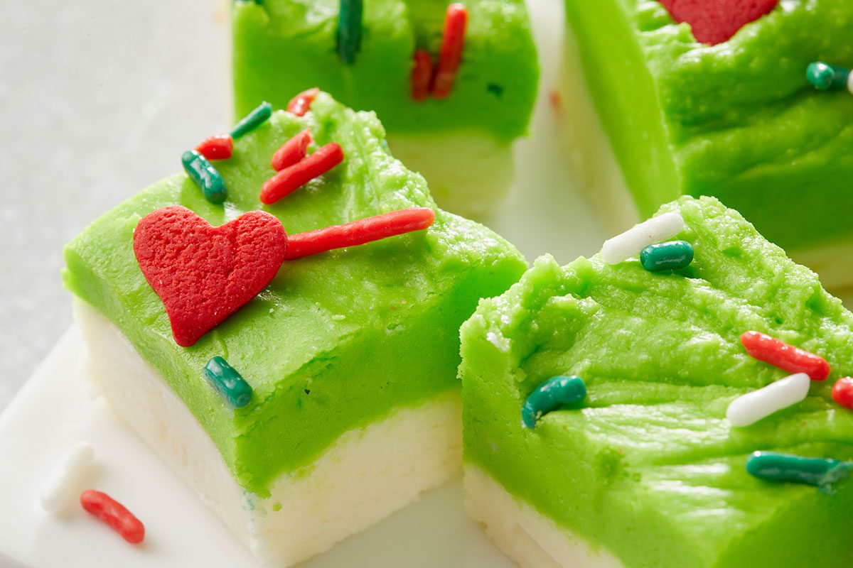 Closeup shot of Squares of white and green layered fudge are topped with red; green and white sprinkles and heart shaped decorations arranged on a white surface