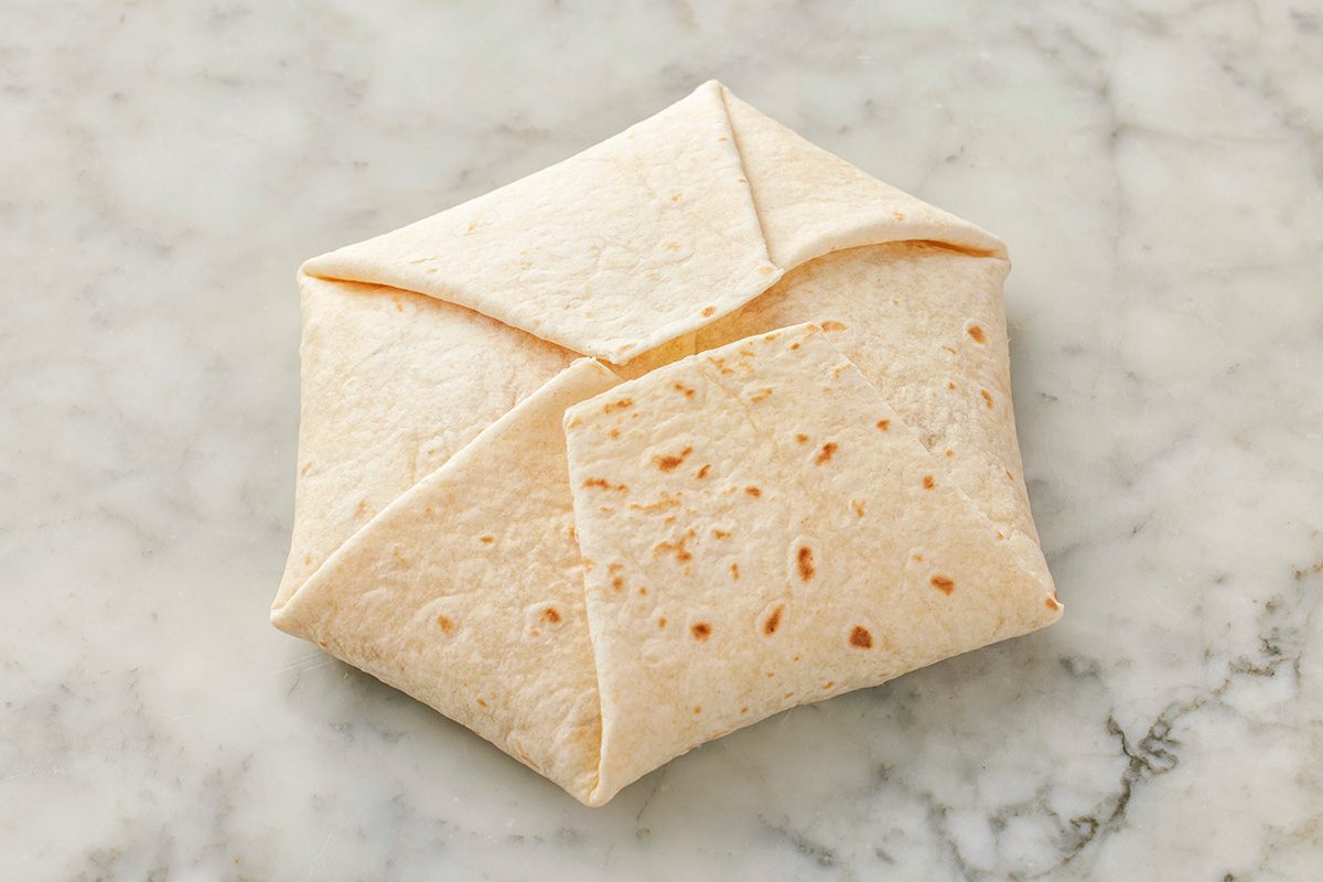 This is a close-up shot; a folded tortilla wrap forms a hexagonal shape; neatly encasing its filling and placed on a light-color marble surface