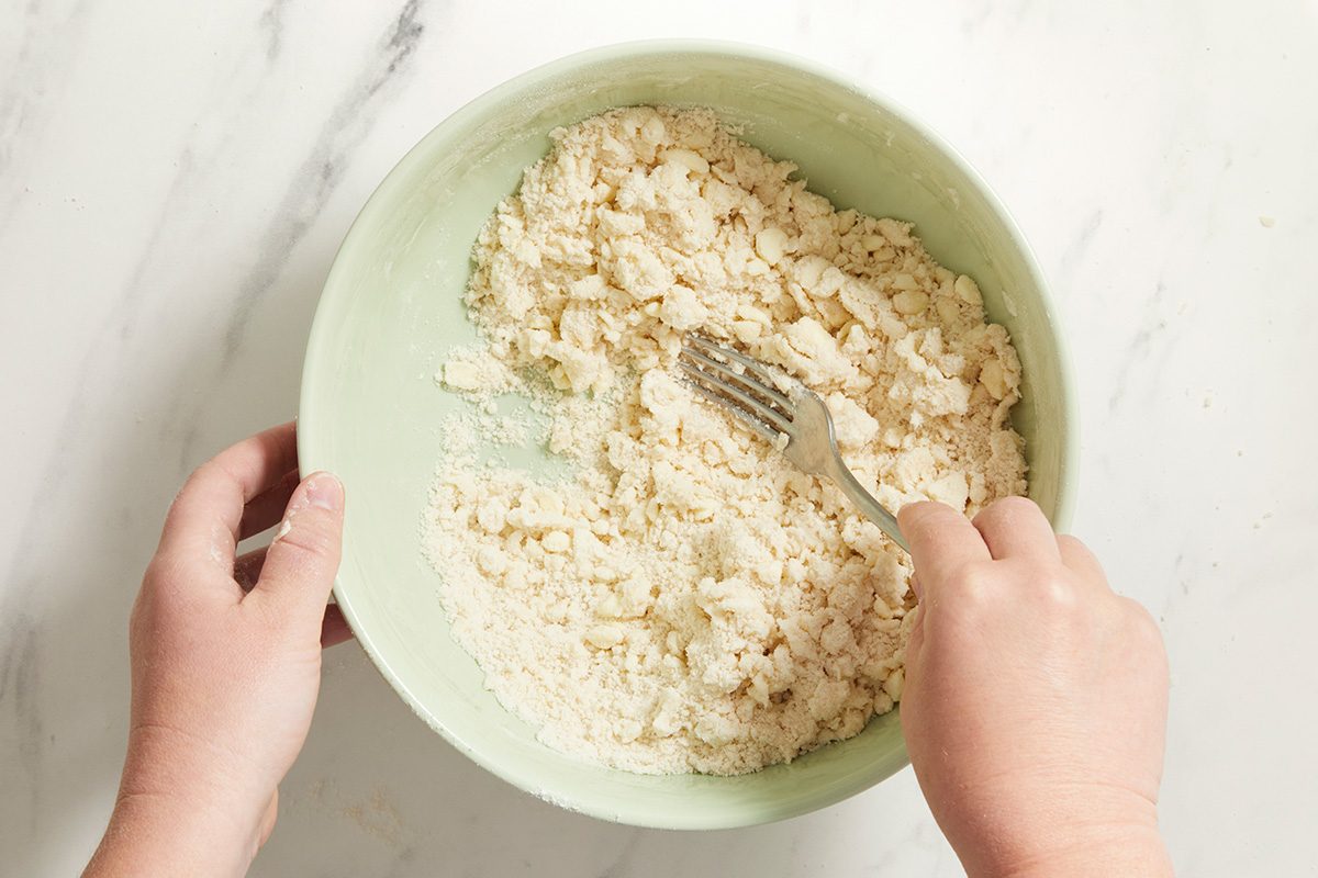 A person holds a bowl of crumbled tofu and mixes it with a fork on a white marble surface.