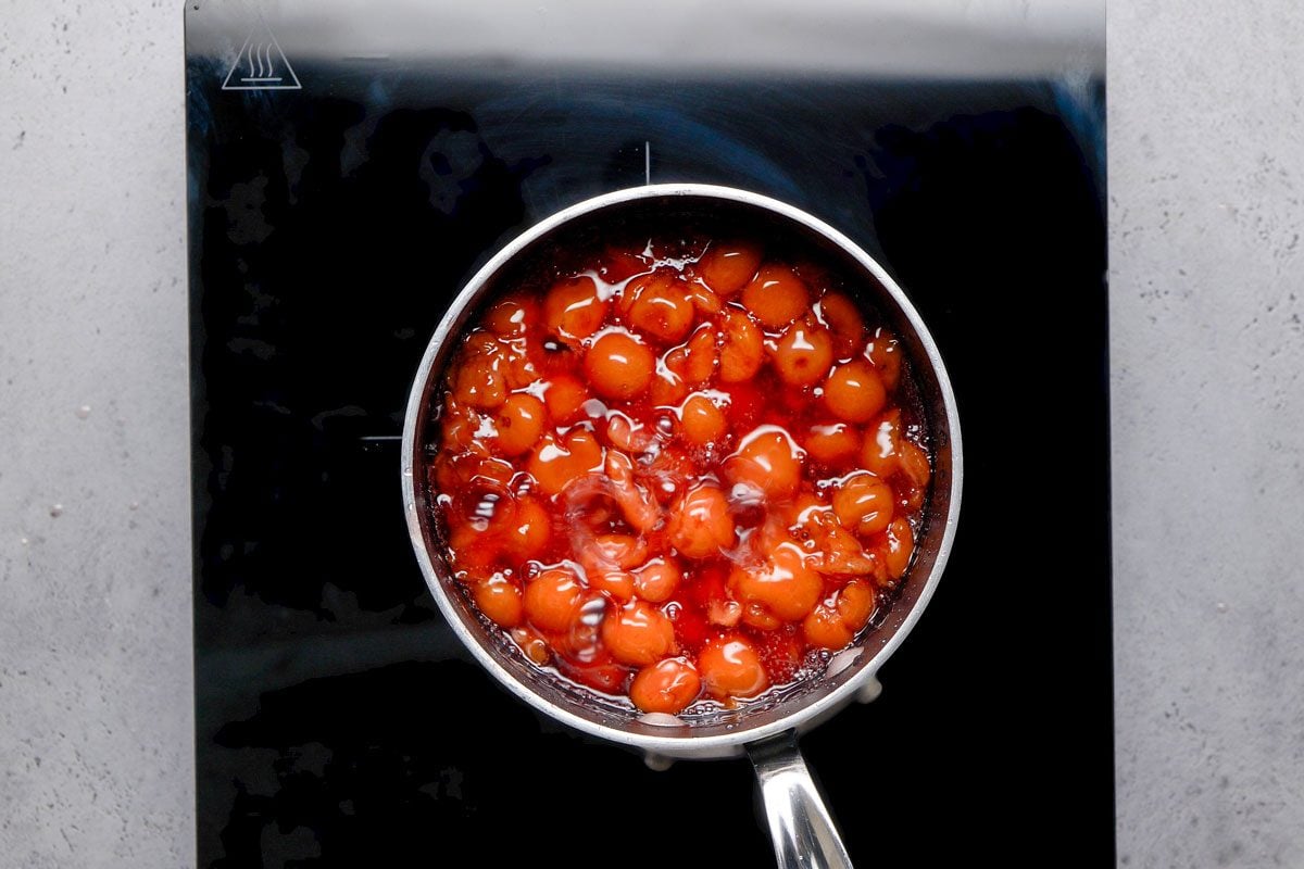 overhead shot of a saucepan filled with bubbling red and brown sauce sits on a black stovetop, viewed from above, The sauce appears to be simmering, with visible bubbles and a glossy surface
