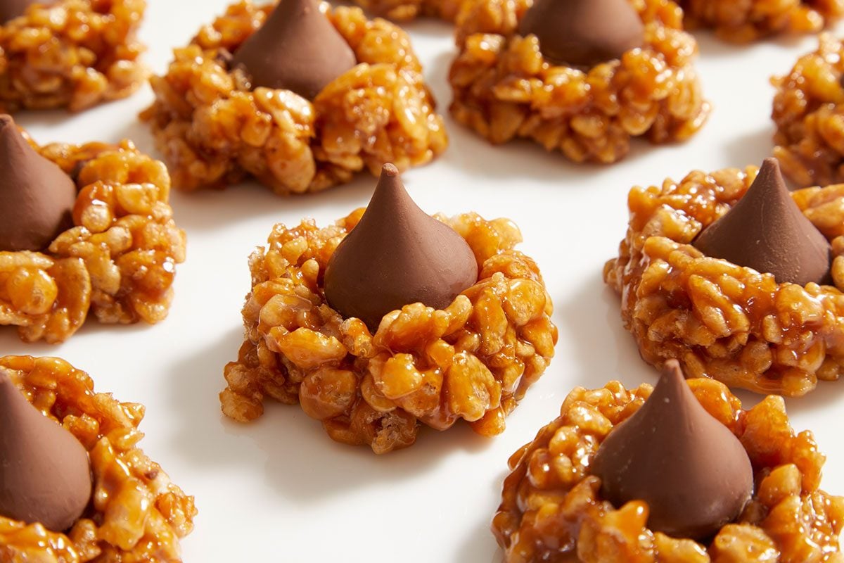 Clusters of caramel-colored Rice Krispies treats, each topped with a single Hershey’s Kiss chocolate, arranged in rows on a white surface.