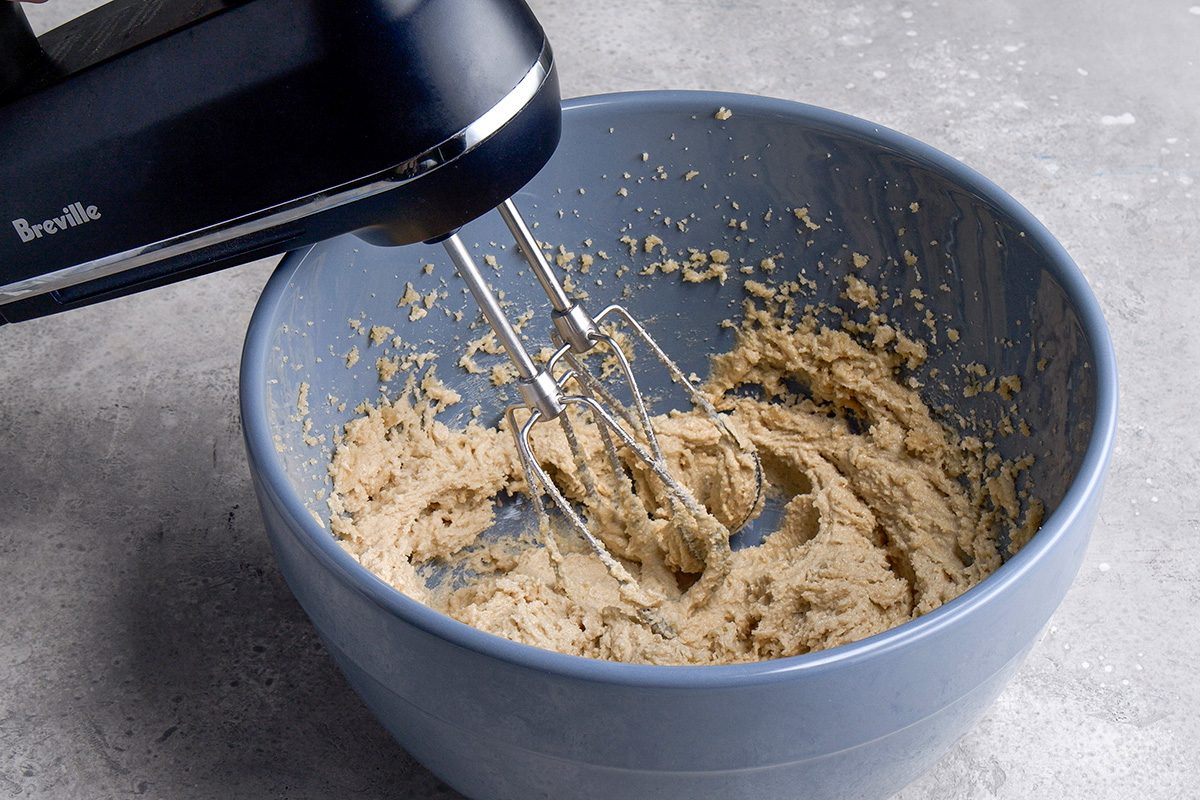 A hand mixer blending a creamy batter in a blue mixing bowl placed on a gray countertop.