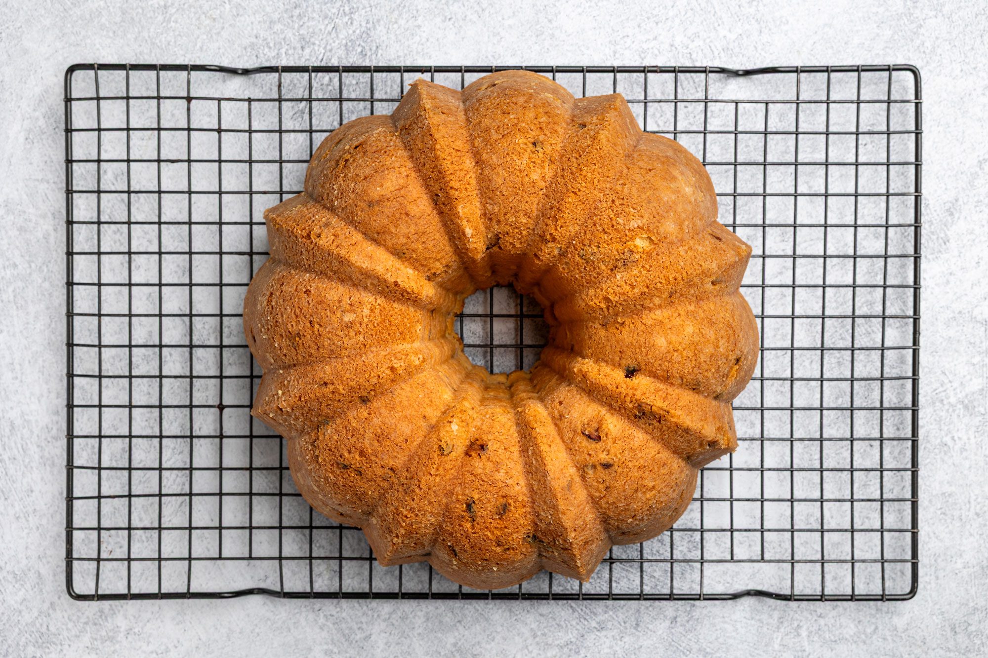 Overhead shot of a golden-brown Bundt cake with a decorative fluted pattern; resting on a black wire cooling rack against a light gray background