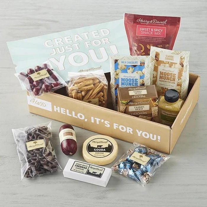 A gift box with snacks, including cheese, sausage, crackers, chocolate, cookies, and snack mix. The box says 