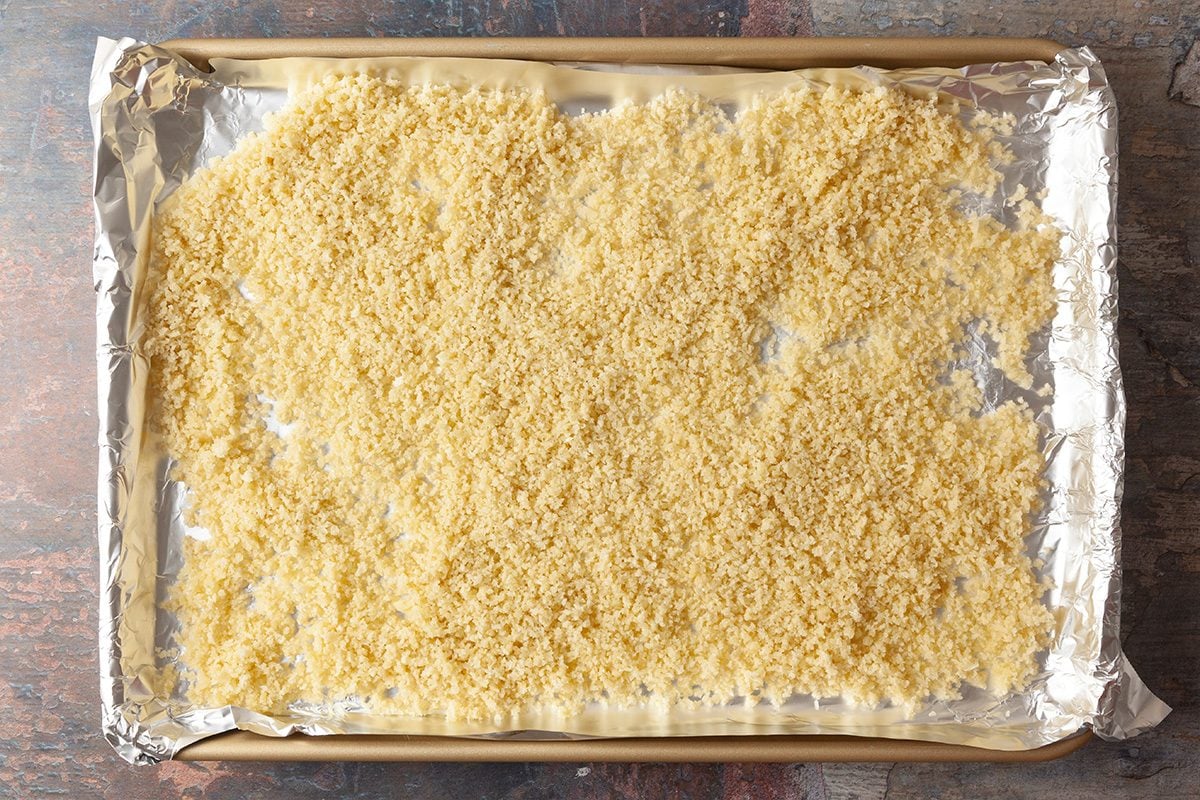 A baking sheet lined with foil is covered with an even layer of uncooked orzo pasta spread out across the surface.
