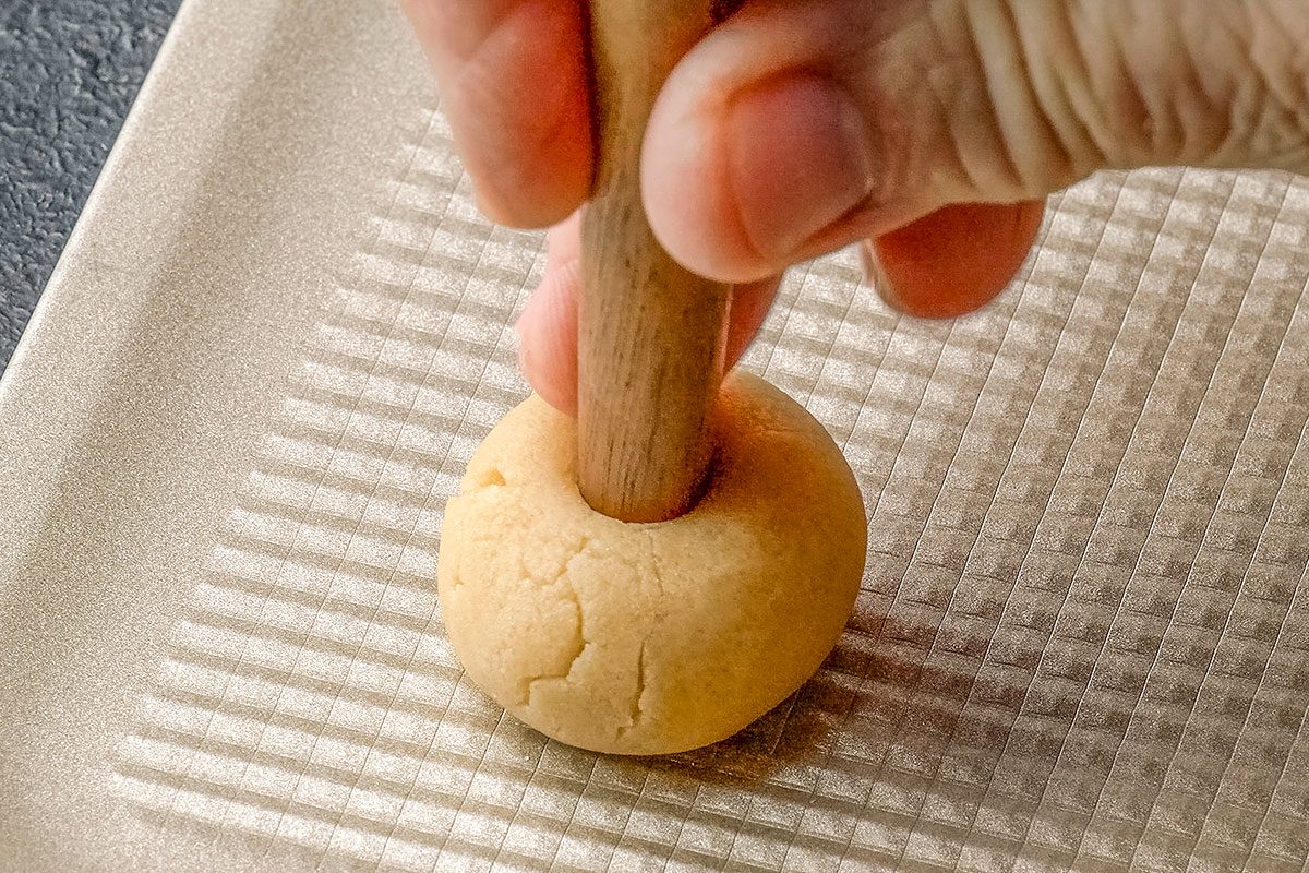 Close-up shot of using the end of a wooden spoon handle; make a 1/2-inch deep indentation in the center of each ball; dark surface