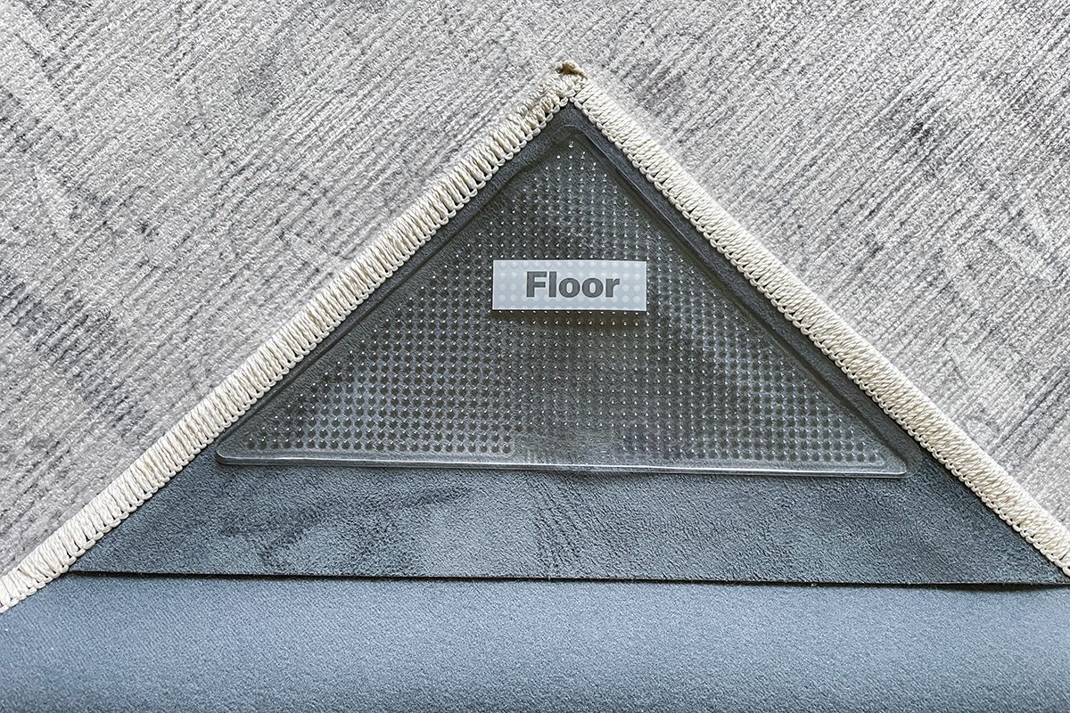 A close-up of the corner of a rug lifted to reveal a triangular label underneath with the word “Floor” printed on it, indicating which side should face down.