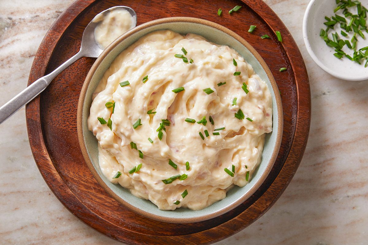 Overhead shot of the Bacon Aioli served in a ceramic bowl, neatly swirled and topped with chopped chives, emphasizing texture and garnish detail.