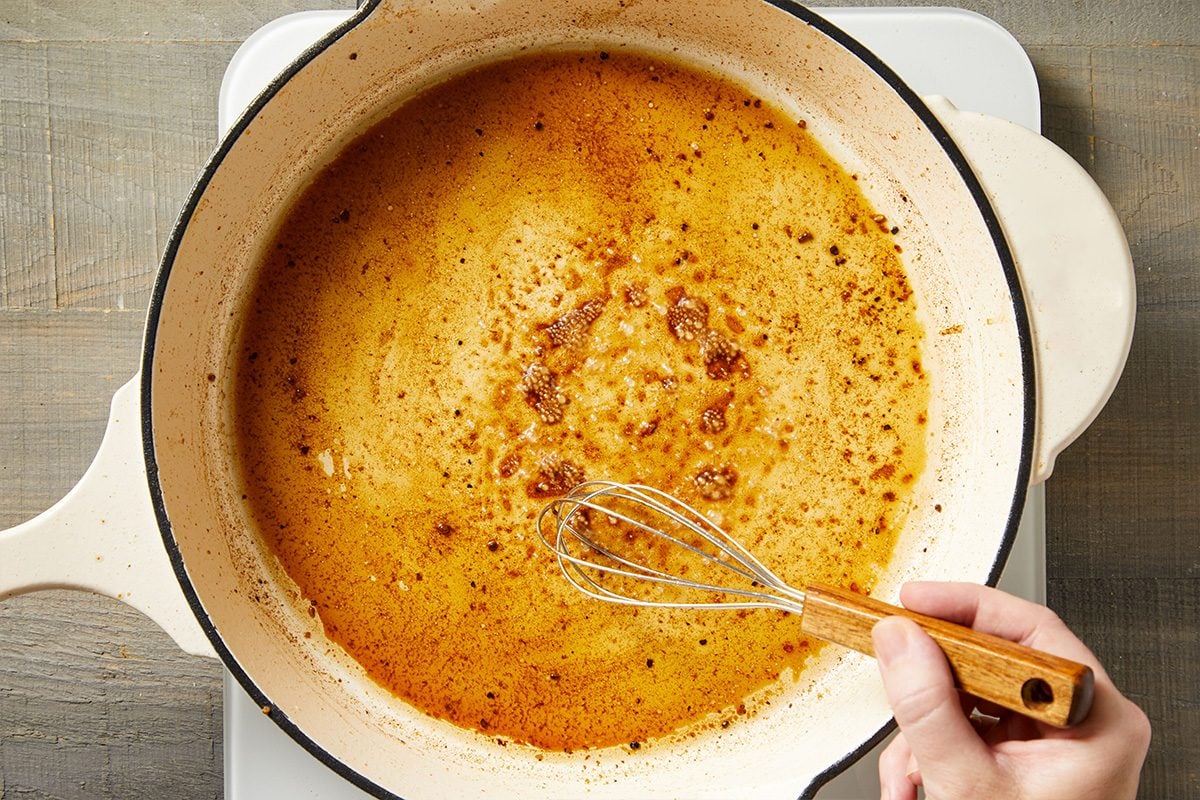 Overhead shot of beef drippings being whisked in a Dutch oven to make gravy base.