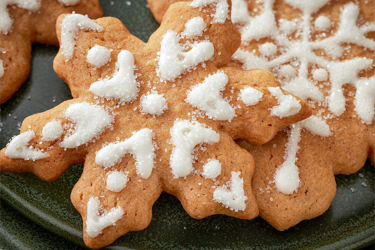 Closeup of butterscotch gingerbread cookies shaped like snowflakes, decorated with white icing and sugar crystals, on a green plate;