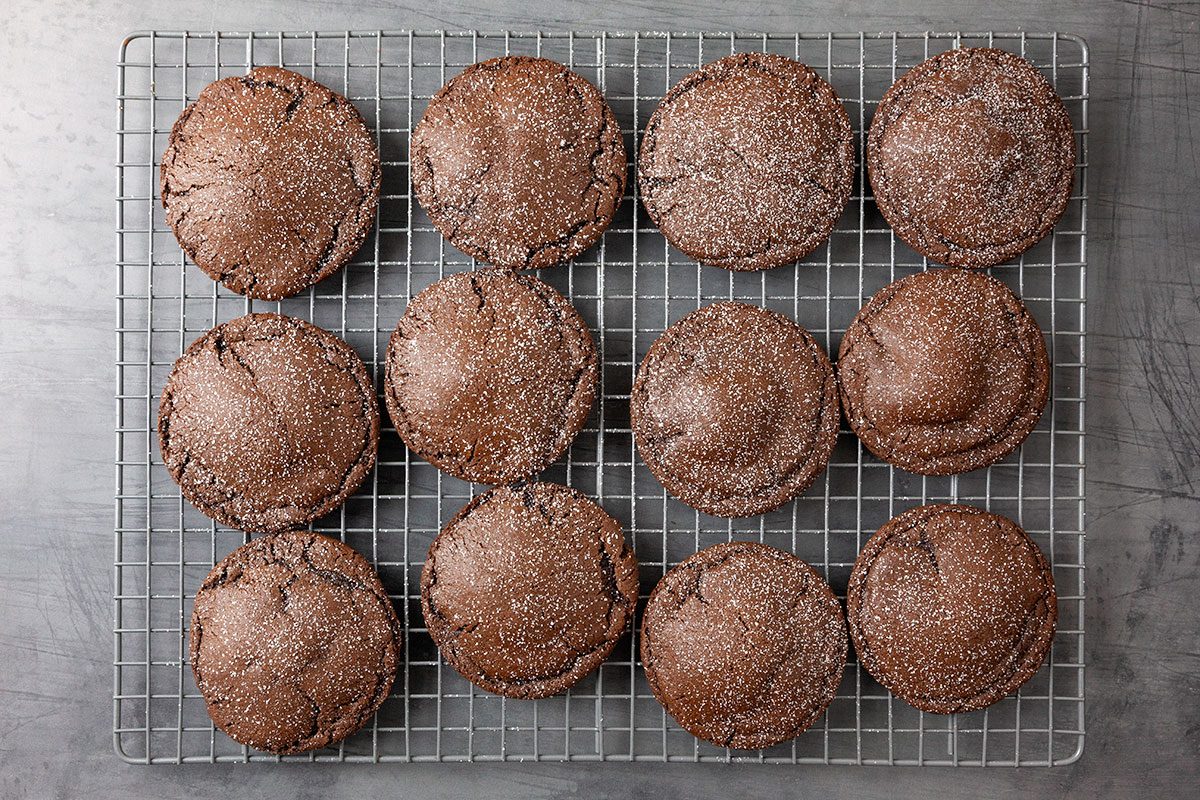 Overhead shot of Chocolate Lava Cookies are arranged in twelve neat rounds on a metal cooling rack on a gray surface they are dusted with sugar