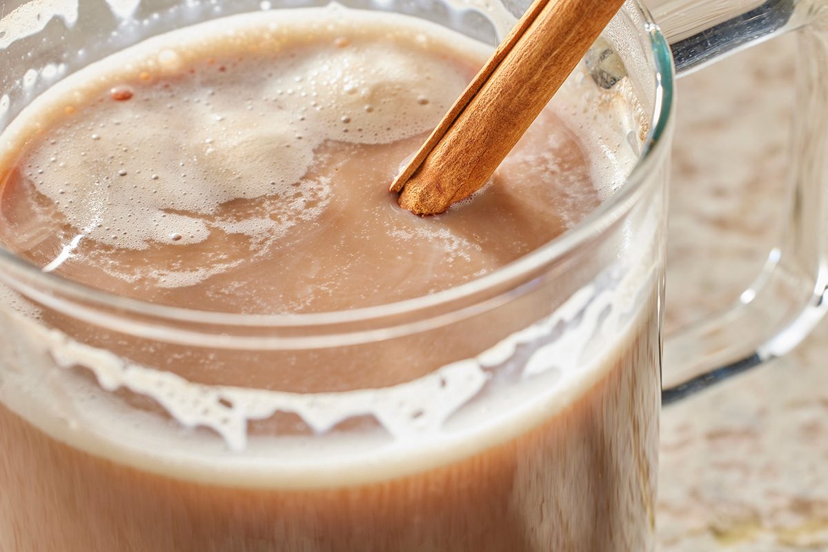 Close-up of a glass mug filled with frothy Cinnamon Mocha Coffee, garnished with a cinnamon stick