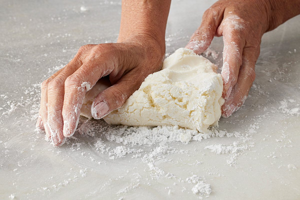 Close-up shot of hands kneading a mound of dough on a floured surface;