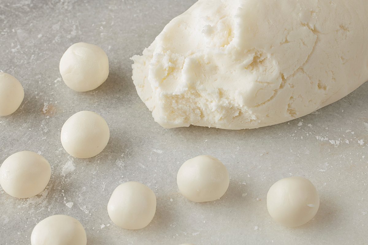 Close-up shot of a chunk of white dough on a floured surface, with several small round dough balls arranged nearby