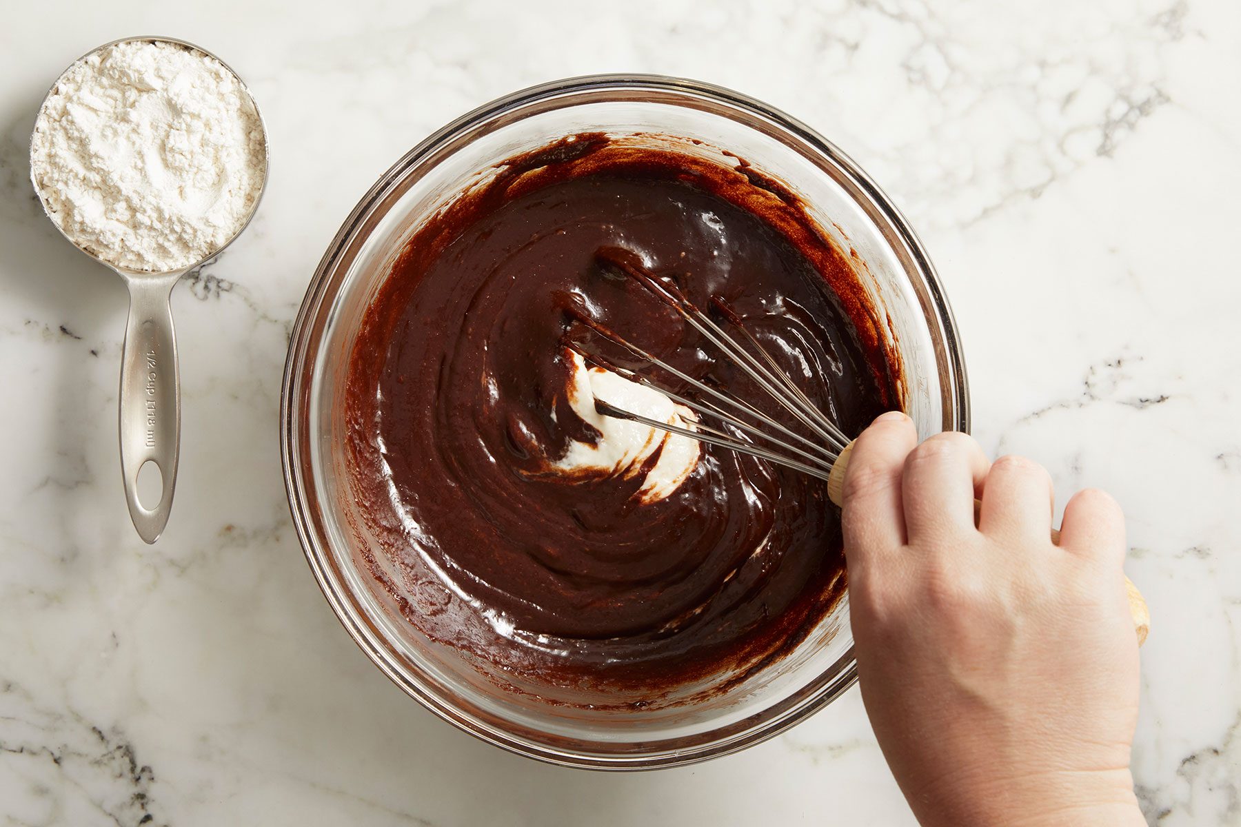 Adding sourdough to the brownie mixture in a glass bowl in small quantities and stirring with a whisk.