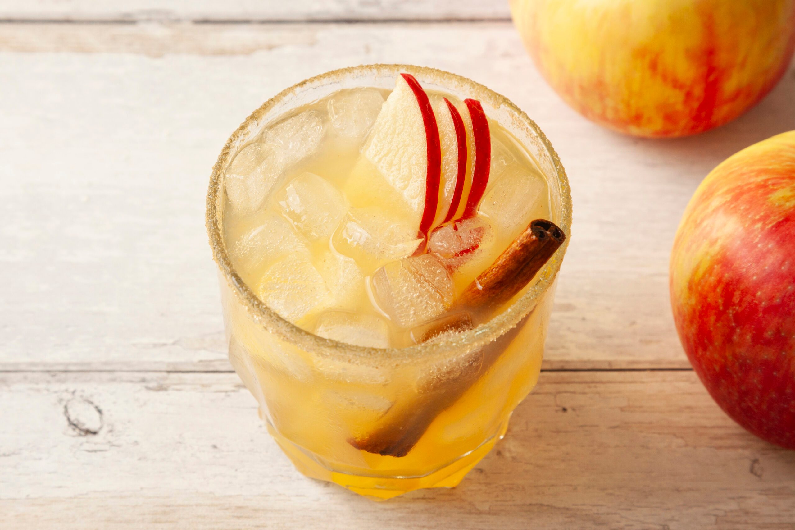 Closeup shot of a Harvest Mezcalita in a glass with ice, red apple slices, and a cinnamon stick