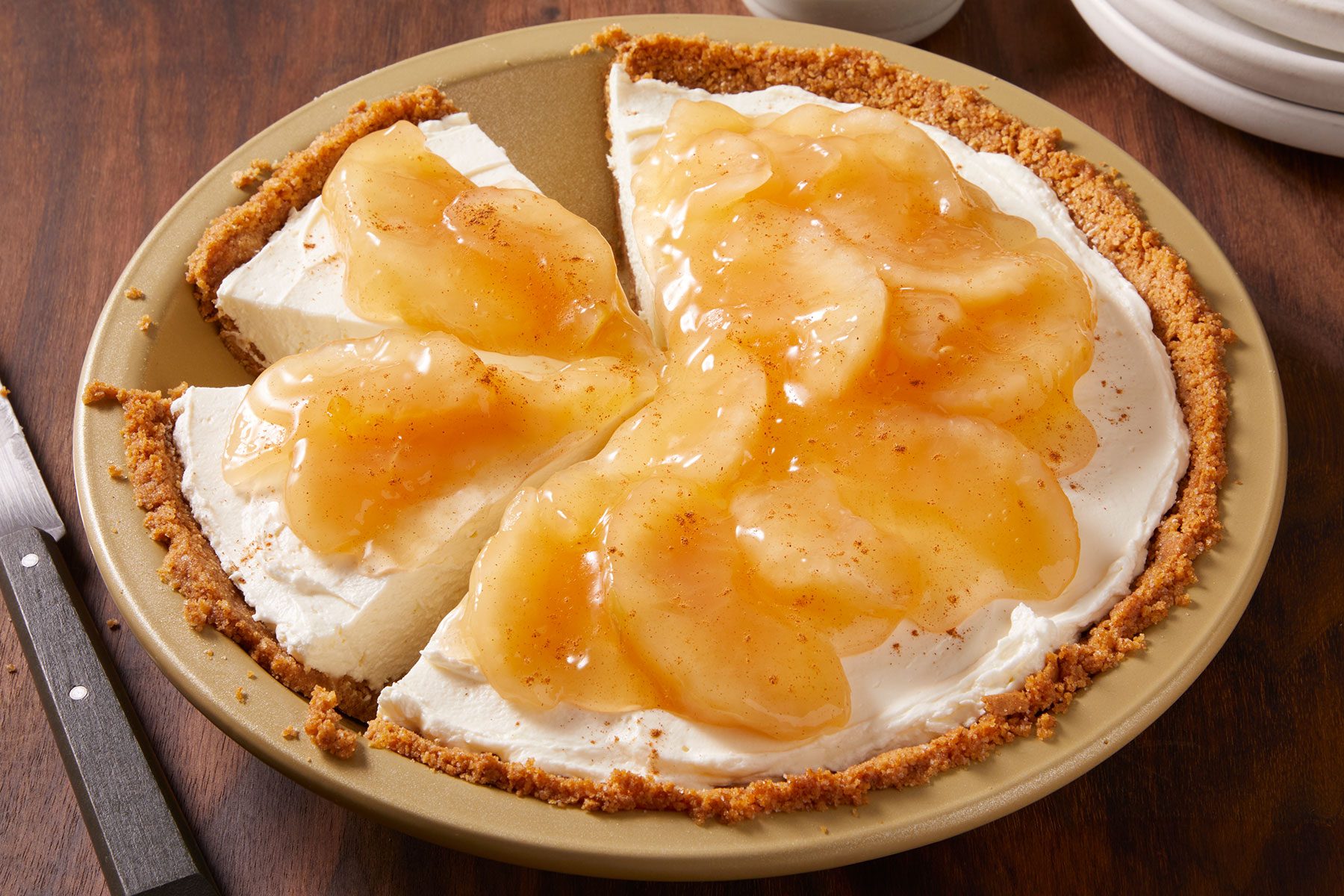 Apple Cream Cheese Pie on a plate cut into few pieces with a knife placed on side and a small bowl of cinnamon.