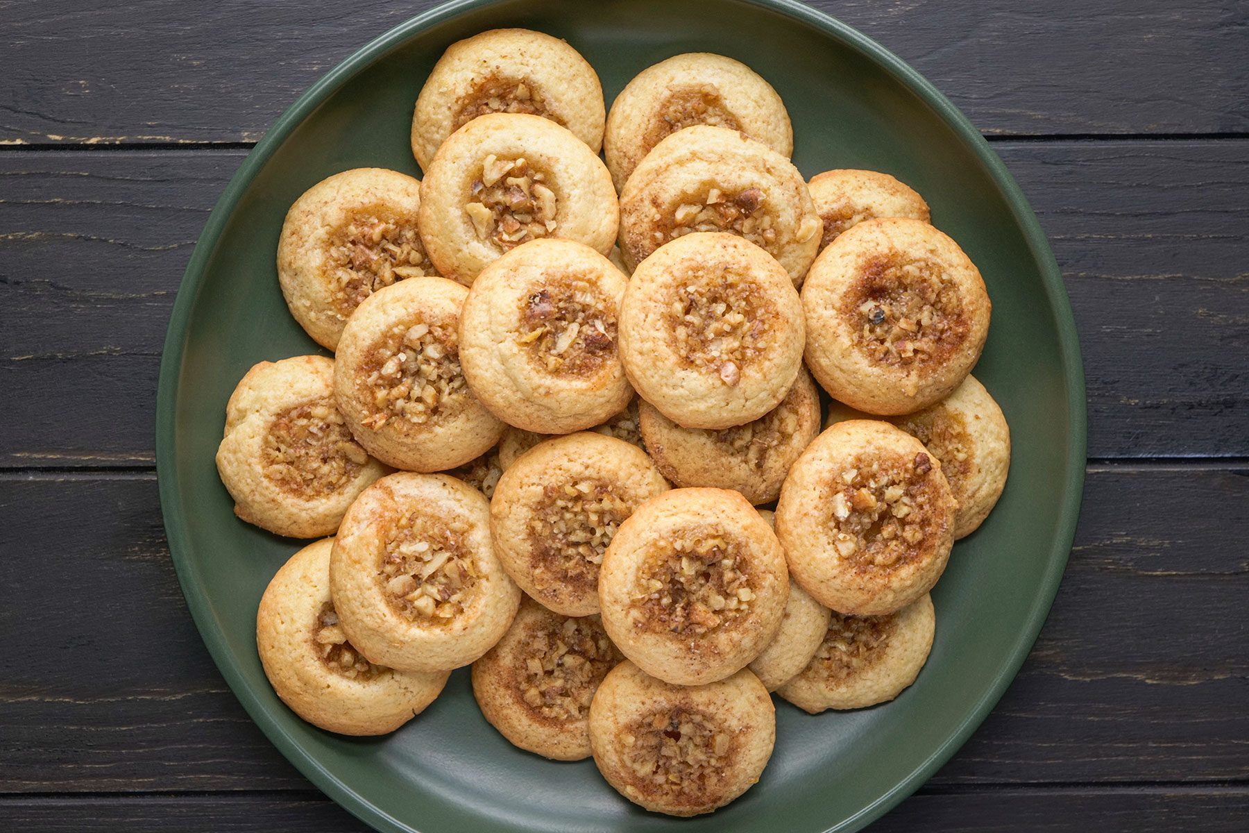 Baklava Thumbprint Cookies in a pile on a green plate on wooden plank table.