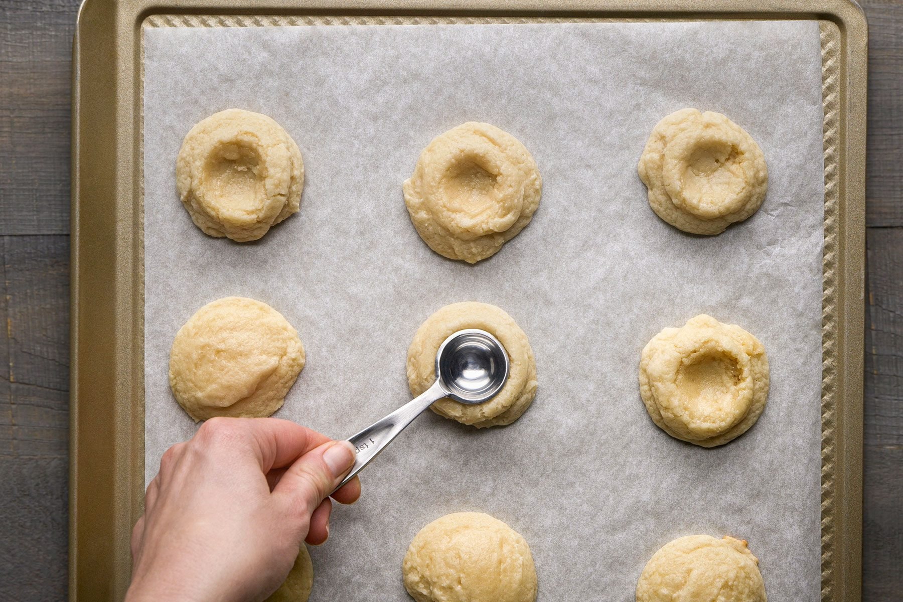 Pressing a deep indentation in the center of each half baked cookie with the back of a rounded teaspoon.