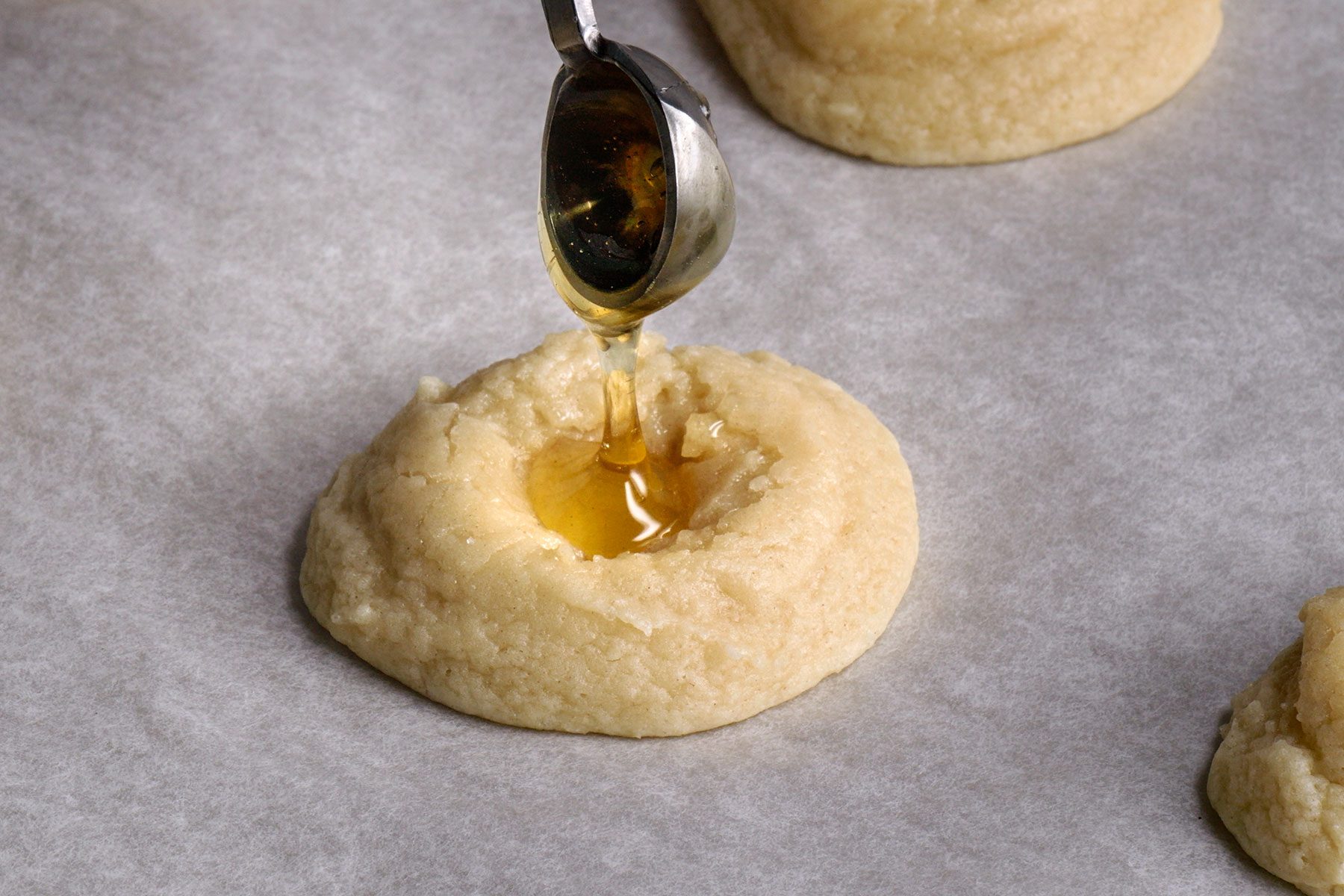 Filling half baked cookie's indentation with the honey using a spoon.