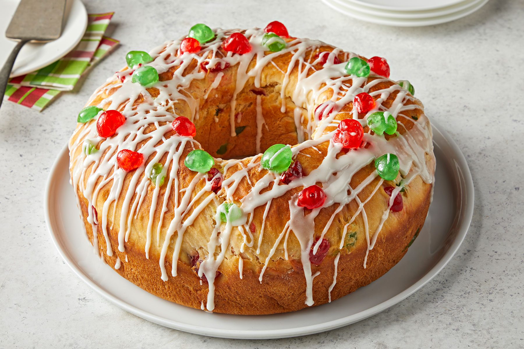 Christmas Bread with drizzled glaze and candied fruits on top in a white plate on a counter.