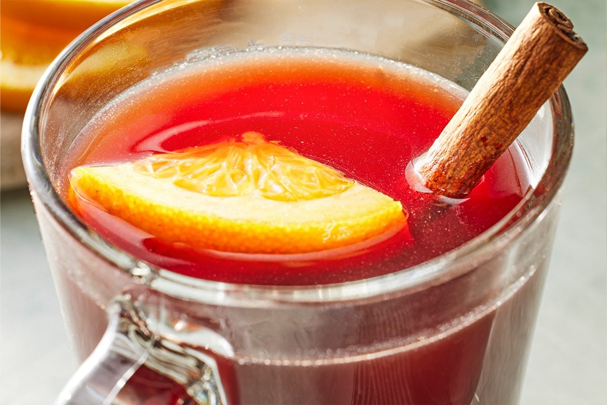 Close-up shot of a mug of Christmas Tea showing a floating orange wedge and cinnamon stick, with a warm golden glow.