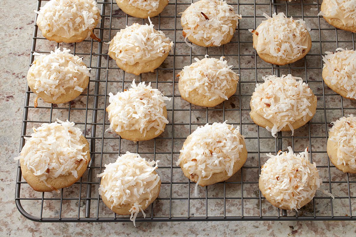 3/4-angle view of Coconut Clouds cookies topped with shredded coconut, lined up on a cooling rack on a speckled countertop;