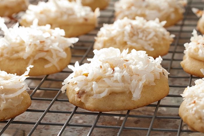 3/4-angle view of Coconut Clouds cookies topped with shredded coconut, lined up on a cooling rack on a speckled countertop;